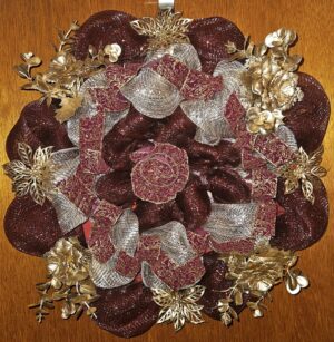 Handmade deep red and gold Christmas wreath with shimmering mesh ribbon, gold floral accents, and festive holiday design on a wooden door