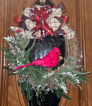 Handmade red cardinal Christmas wreath on grapevine base with evergreen foliage, pinecones, white berries, and a red glitter and plaid bow on a front door