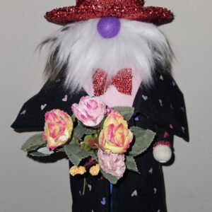 Handmade 20-inch Valentine's Day gnome named Ernest with sparkling red sequin top hat, long white fluffy beard, purple nose, black heart-patterned coat, red glitter bow tie, and holding a bouquet of pink and yellow roses.