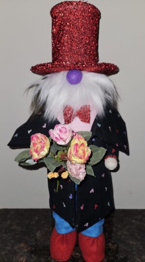Handmade 20-inch Valentine's Day gnome named Ernest with sparkling red sequin top hat, long white fluffy beard, purple nose, black heart-patterned coat, red glitter bow tie, and holding a bouquet of pink and yellow roses.