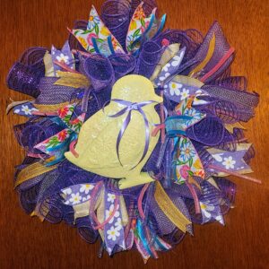 Welcome spring in cheerful style with this 20-inch Easter Chick Wreath. Designed in soft pastels and vibrant purples, this round wreath creates an eye-catching focal point for your front door, entryway, or interior wall. Layers of rich purple deco mesh form a full, lush base that gives this wreath beautiful volume and texture. Throughout the design, patterned ribbons in floral prints, daisies, gold accents, and soft pastel tones add depth and movement. Pops of pink, yellow, and blue bring the entire piece to life while keeping the look fresh and seasonal. At the center, an adorable yellow chick takes the spotlight. Finished with delicate glitter detailing and a soft lavender bow, the chick adds charm and personality without overwhelming the design. The combination of bold purple mesh and gentle spring colors makes this wreath stand out beautifully against neutral or brightly painted doors. Measuring approximately 20 inches round, this Easter Chick Wreath is perfectly sized to make a statement while still fitting standard doors comfortably. It works wonderfully for Easter celebrations, spring gatherings, church events, or simply welcoming guests with festive seasonal décor. Each wreath is carefully handcrafted with attention to detail and quality materials to ensure it holds its shape and beauty throughout the season. Hang it on your front door, above a mantel, or as part of your Easter decorating theme. Add a playful yet elegant touch to your home this spring with this vibrant 20-inch Easter Chick Wreath.