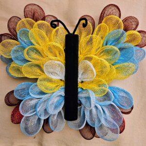 Handmade deco mesh butterfly wreath in vibrant yellow, blue, white, and maroon colors with black fleece body and curled antennae, 16x18 inches, displayed flat on a neutral background.