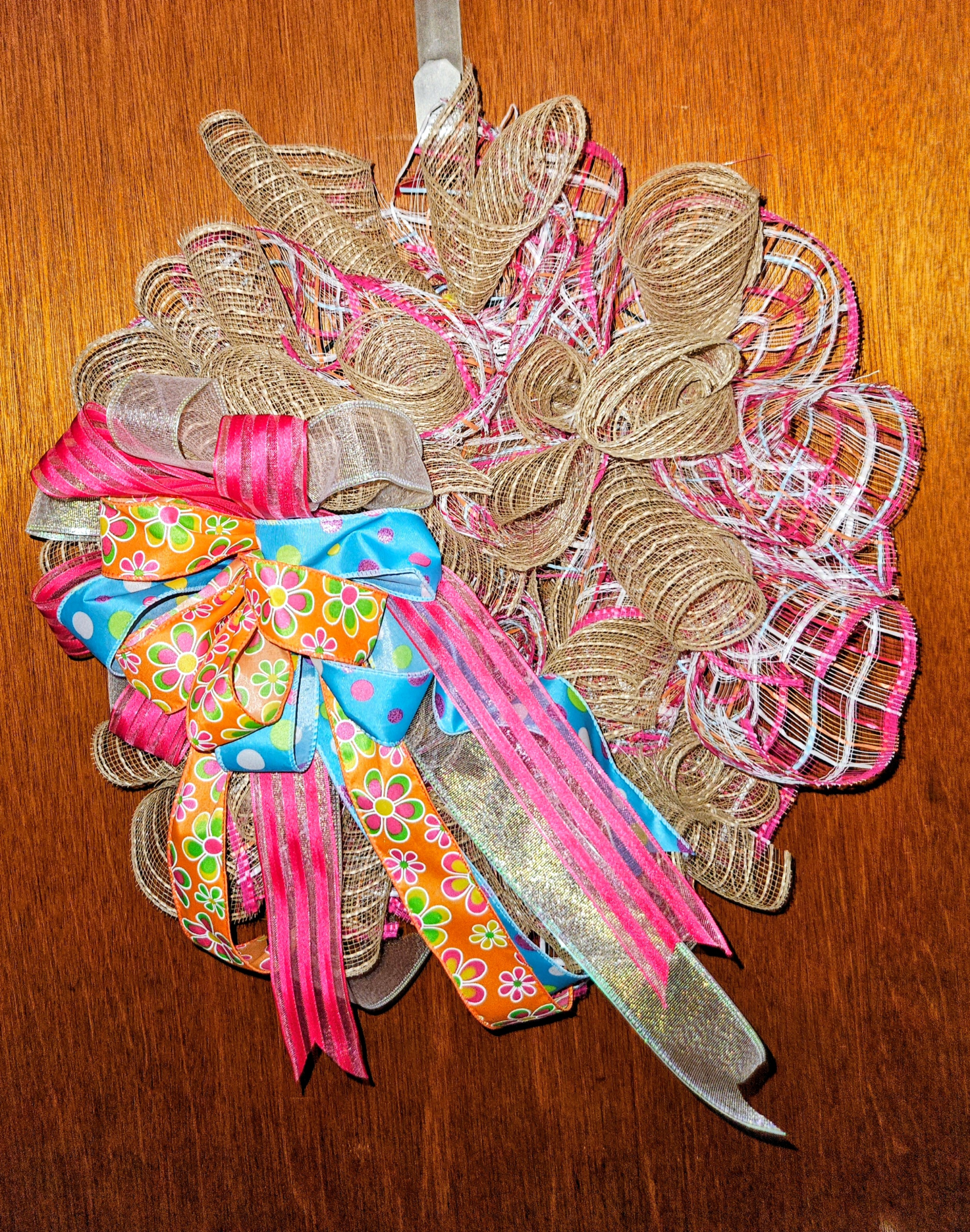 Close-up of a large handmade Sherbet Colors wreath featuring orange floral ribbon, blue polka dot ribbon, hot pink stripes, iridescent shimmer, burlap and mesh layers with a dramatic bow on a wooden door background.