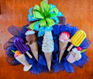 Colorful handmade ice cream wreath with plush cones, popsicles, blue mesh base, and bright polka dot bow