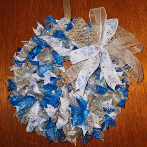 Blue white and gold snowflake wreath with glitter ribbons and large metallic bow on wooden door