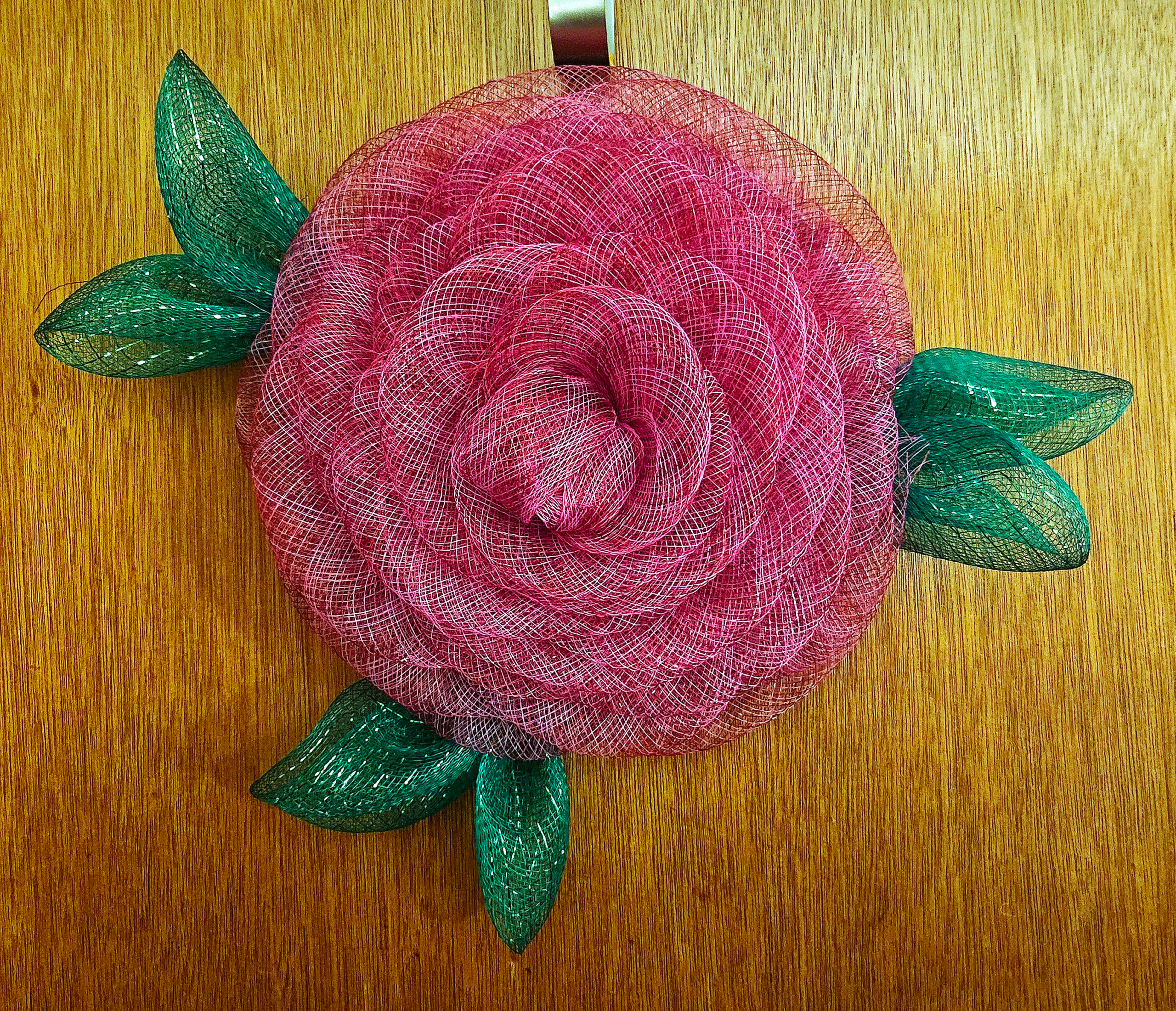 Handmade fuchsia rose wreath with green leaves on wooden door