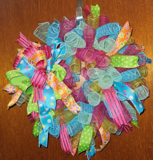Handmade Let's Celebrate wreath bursting with colorful ribbons, mesh, polka dots and patterns on a wooden door