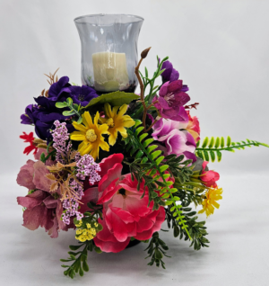 Handmade spring floral candle holder centerpiece with colorful pink, purple, and yellow flowers surrounding a glass hurricane vase.