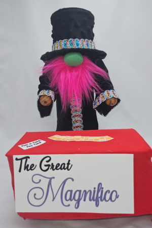 Handmade magician gnome named The Great Magnifico standing behind a magic table with playing cards.