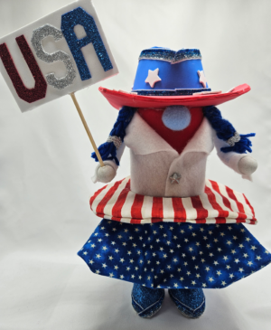 Handmade USA Cowgirl Gnome 11.25 inches tall wearing patriotic stars and stripes dress, blue cowgirl hat with stars, holding glitter USA sign