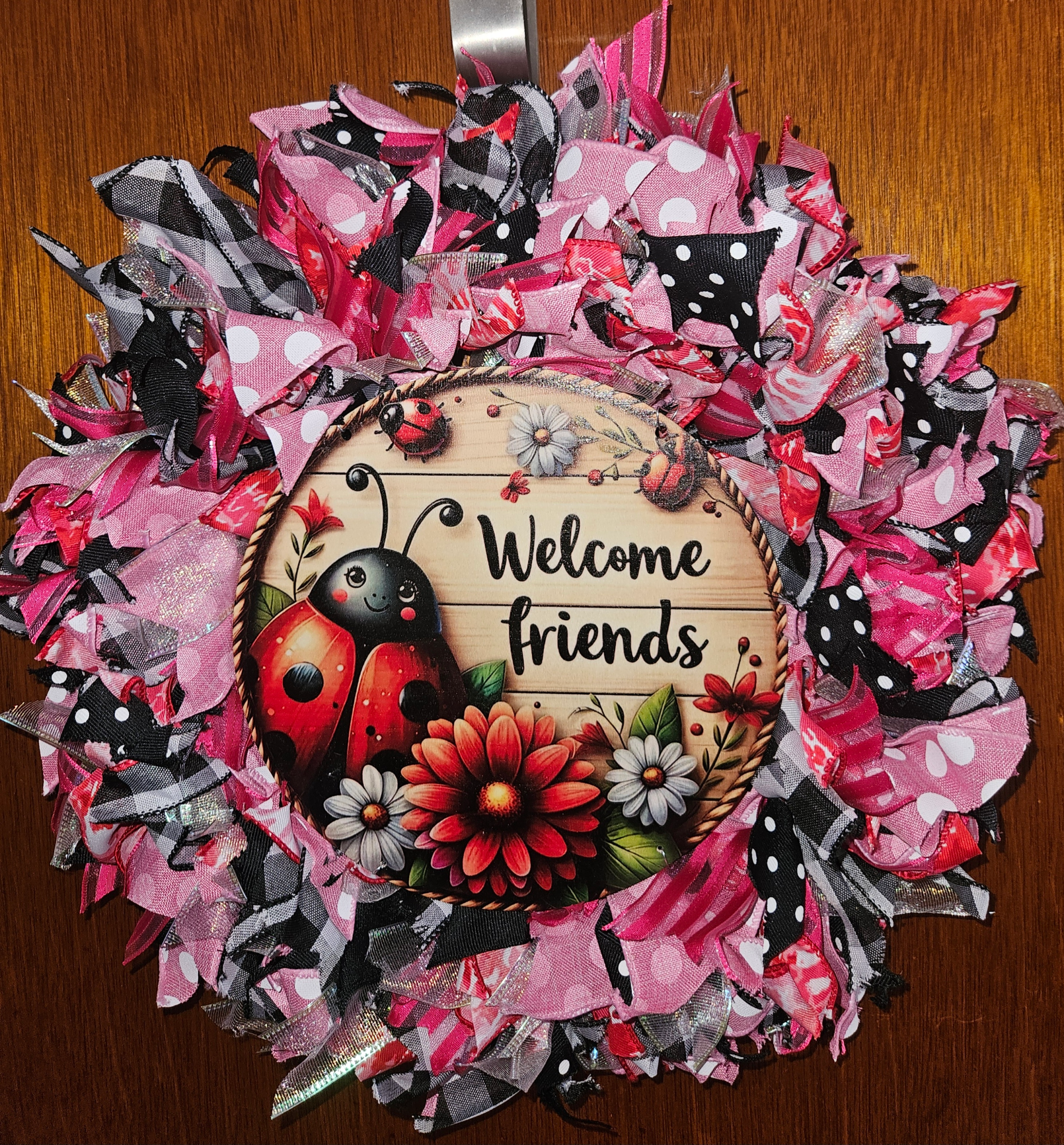 Handmade ladybug ribbon wreath featuring pink patterned ribbons and a Welcome Friends ladybug sign with flowers.