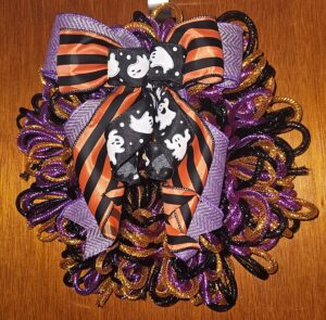 Handmade Halloween mesh tubing wreath in purple, orange, and black featuring a ghost and striped ribbon bow.