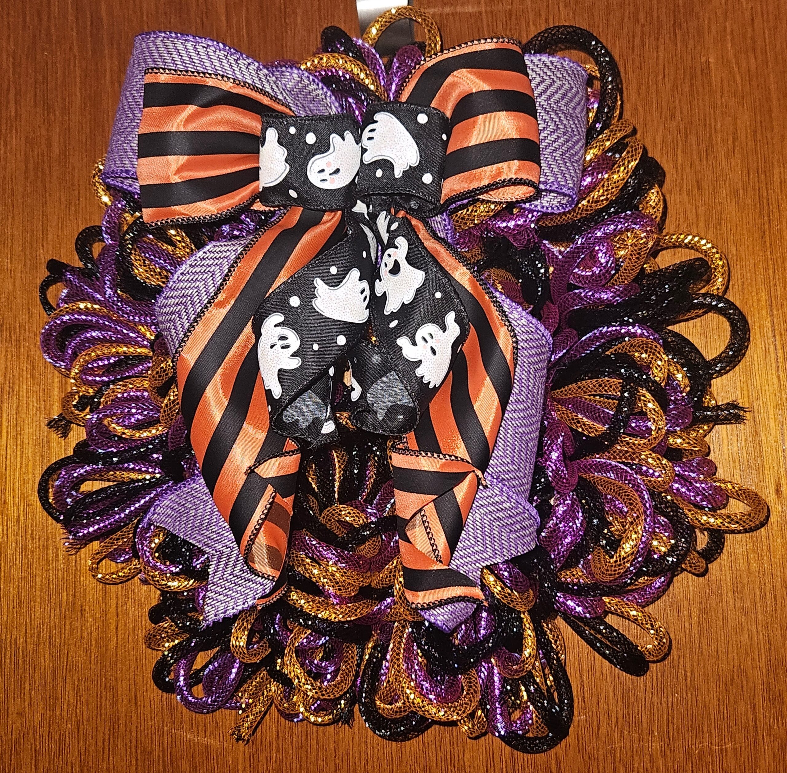 Handmade Halloween mesh tubing wreath in purple, orange, and black featuring a ghost and striped ribbon bow.